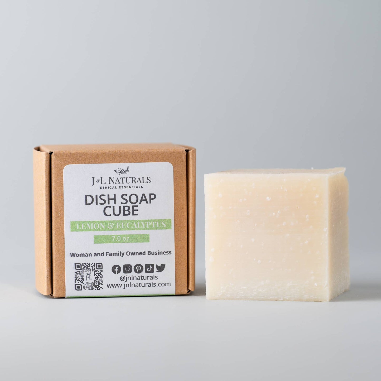 A J&L Naturals Dish soap cube sitting outside its box to show its creamy color and the minimalist and biodegradeable packaging