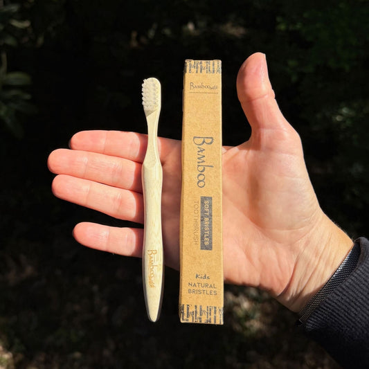 Bamboo Switch kids toothbrush and kraft paper box on an open palm, showing child-size handle length