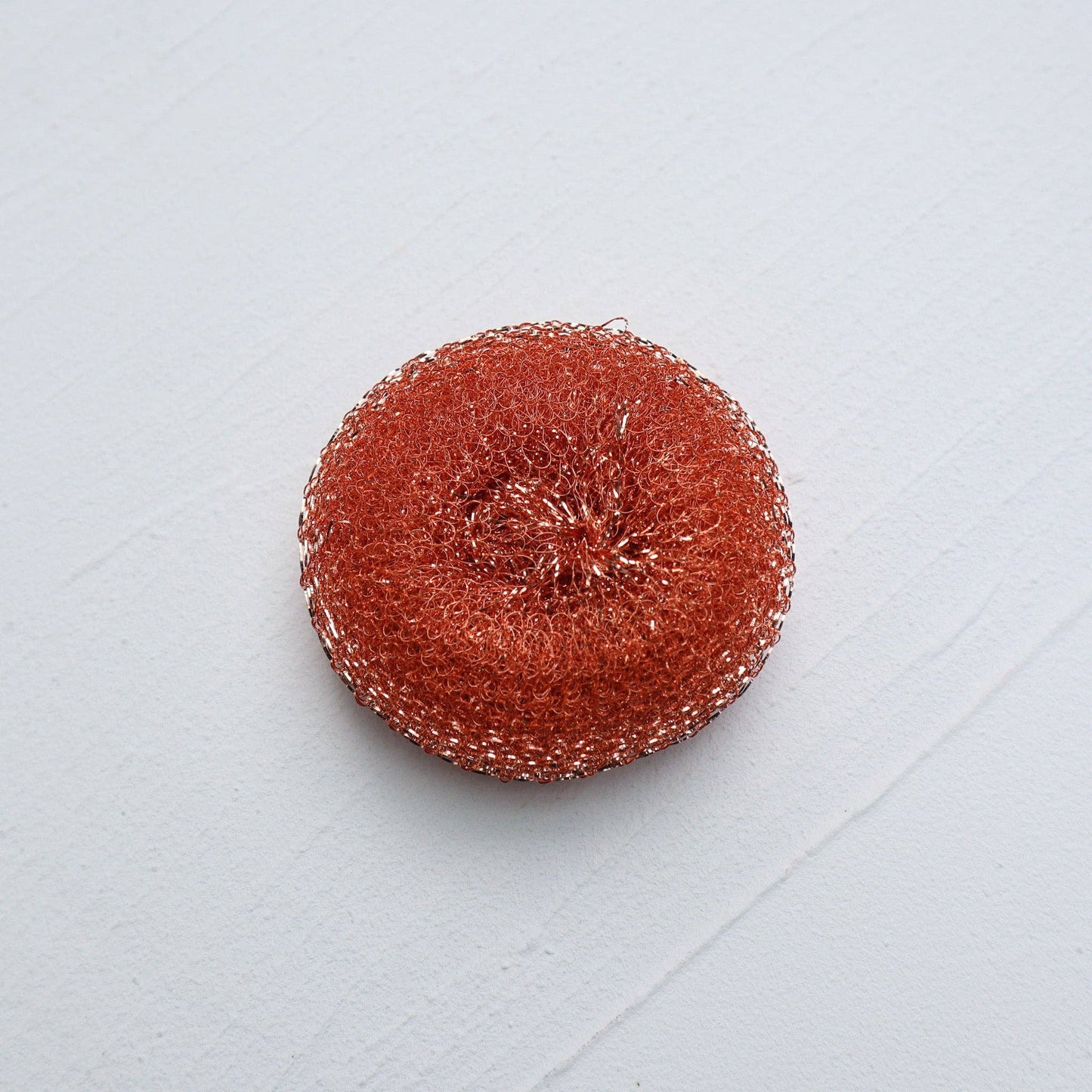 round copper pot scrubber on white surface