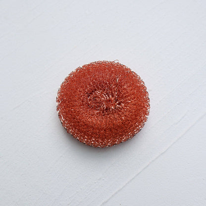 round copper pot scrubber on white surface