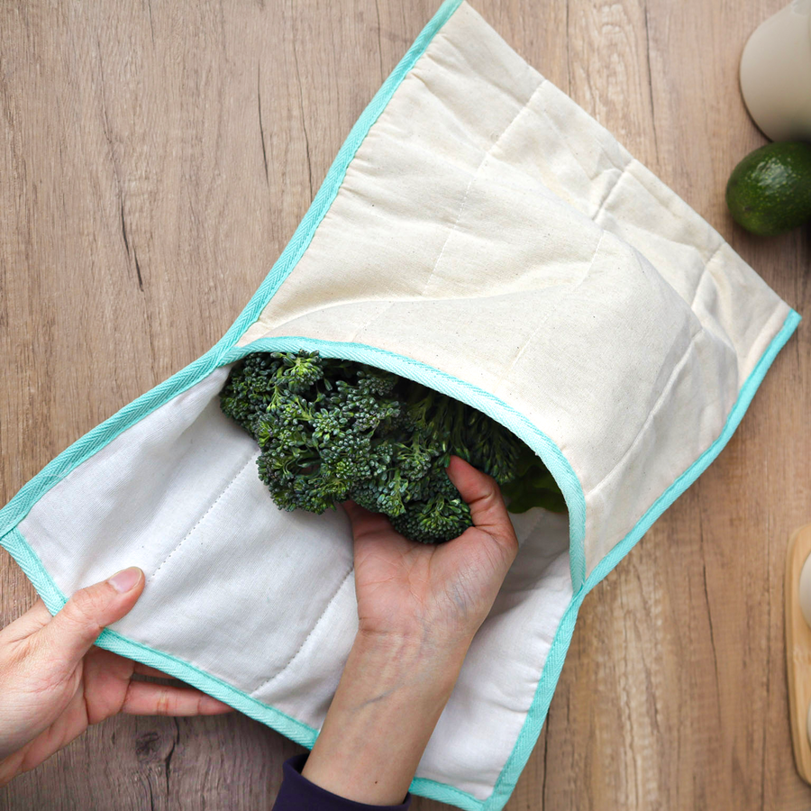 White quilted produce bag with turquoise trim with broccoli in it on a wood table