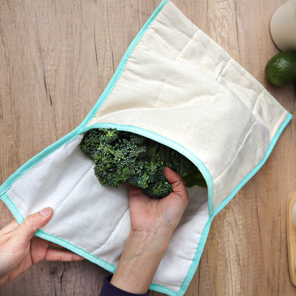White quilted produce bag with turquoise trim with broccoli in it on a wood table