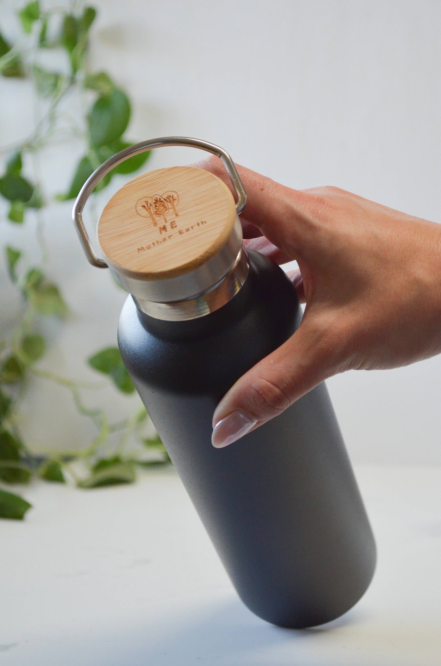 Matte black insulated stainless steel water bottle with an engraved bamboo lid held in a hand.