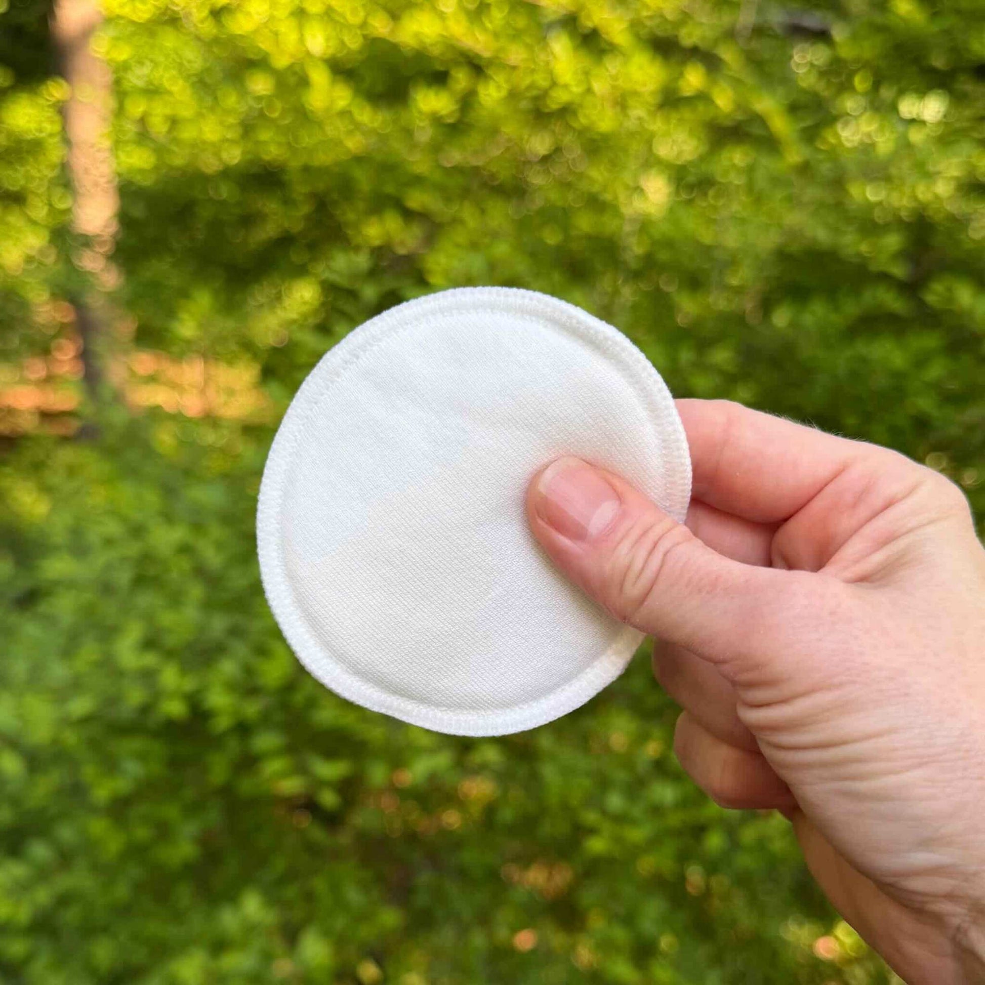 white cotton round being held up with green trees in background