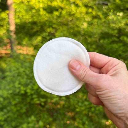 white cotton round being held up with green trees in background