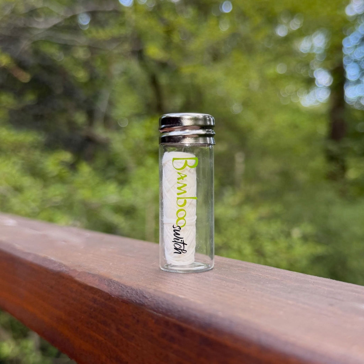 Bamboo Switch white dental floss in a refillable glass jar with stainless steel lid on a wooden railing