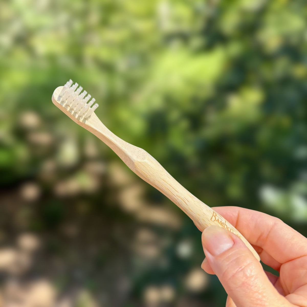 Hand holding a Bamboo Switch kids bamboo toothbrush with soft castor bean oil bristles and contoured handle