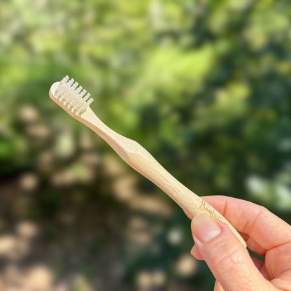 Hand holding a Bamboo Switch kids bamboo toothbrush with soft castor bean oil bristles and contoured handle