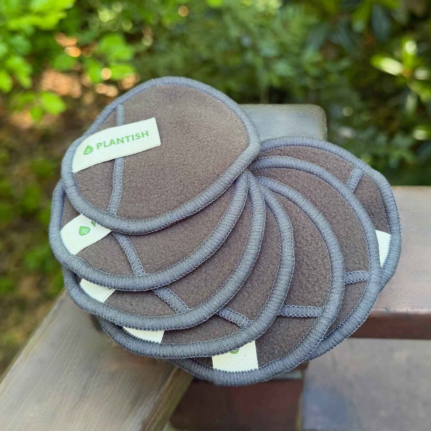 Stack of gray reusable pads with a visible Plantish brand label on a wooden surface outdoors.