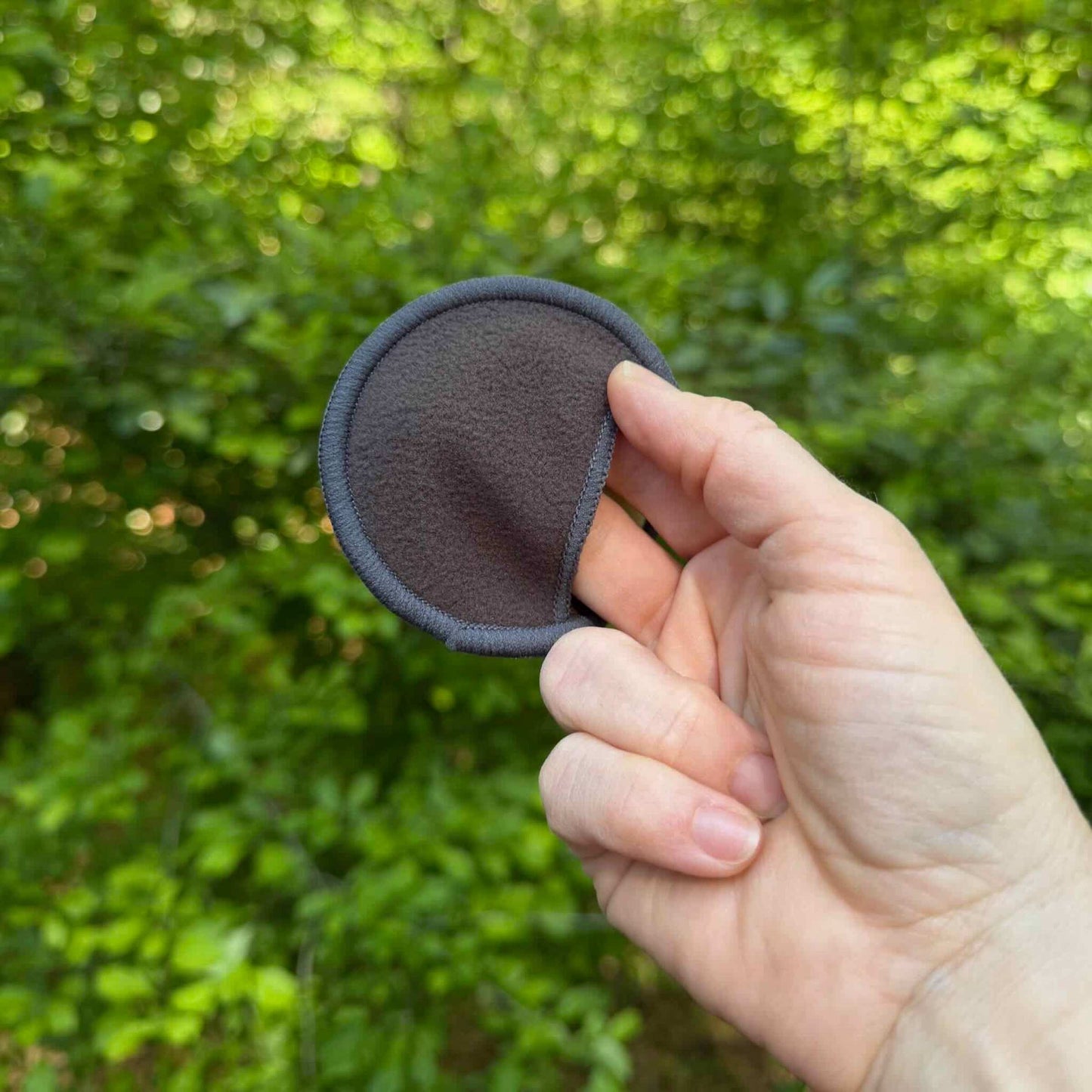 fingers in a bamboo charcoal round's pocket with green trees in background