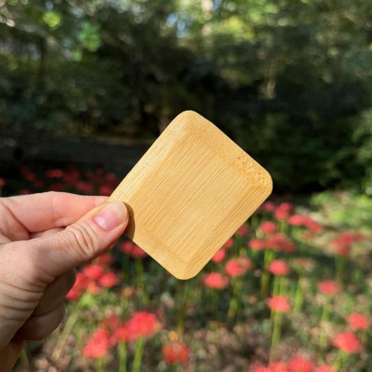 Hand holding a square bamboo pot scraper with rounded corners, showing the natural bamboo grain