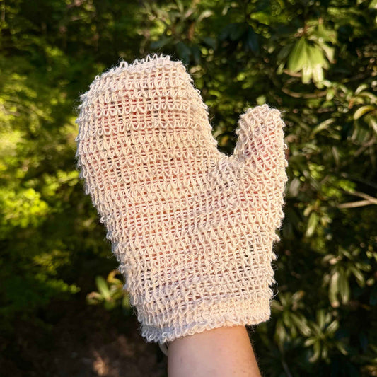 Natural sisal exfoliating shower glove worn on hand outdoors against greenery
