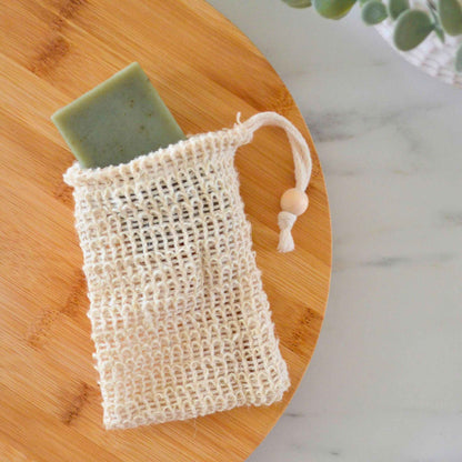 Green natural bar soap sliding into a textured sisal soap saver pouch on a round bamboo tray.