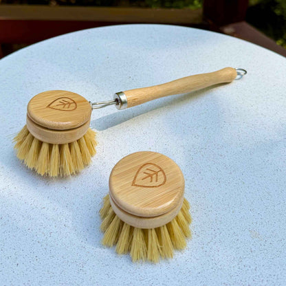 Sisal bamboo dish brush with wooden handle beside a replacement brush head on a white stone table