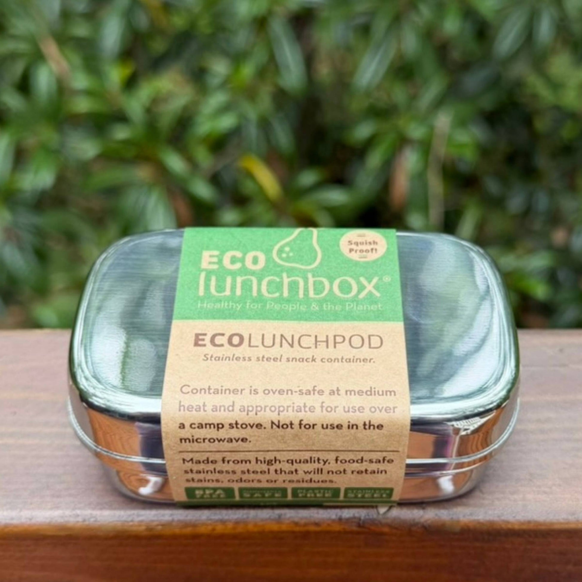 ECOlunchbox stainless steel snack container with a paper product label on a wooden ledge.