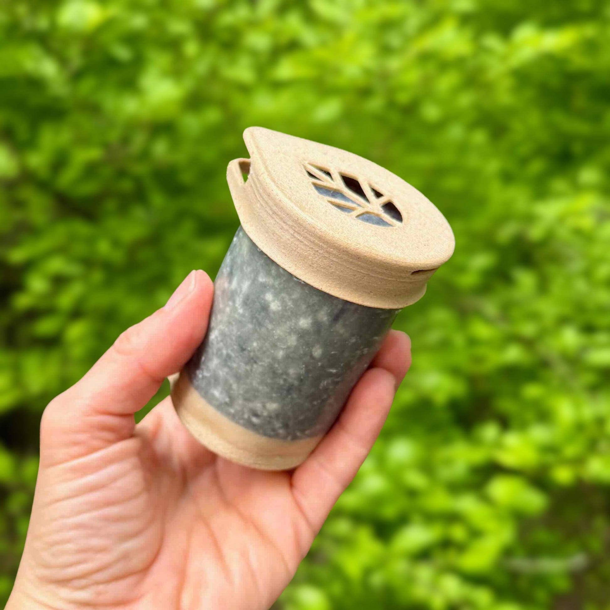 Hand holding cylindrical plastic-free Swell Labs Stem shampoo bar with a smooth purple-black surface and compostable lid