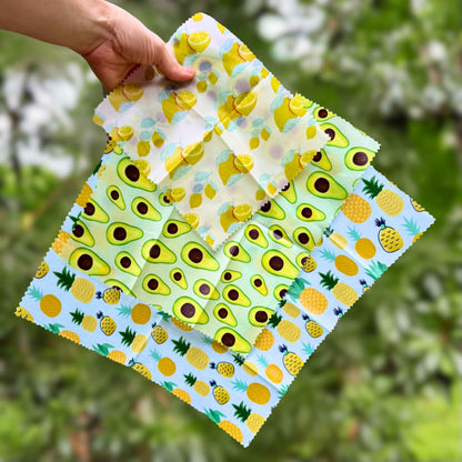 Hand holding a folded reusable wax food wrap with pineapple and avocado print, plastic-free food storage alternative.