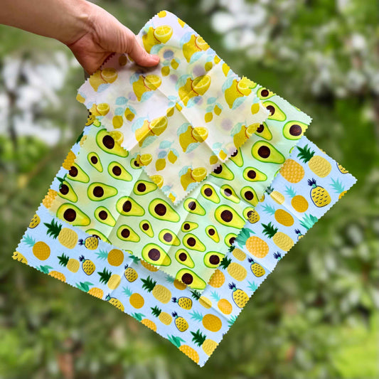 Hand holding a folded reusable wax food wrap with pineapple and avocado print, plastic-free food storage alternative.
