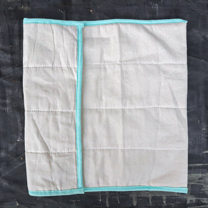 White quilted produce bag with turquoise trim folded on a black surface