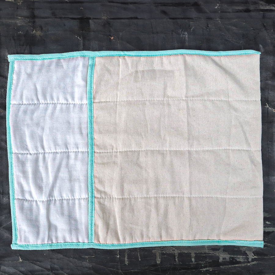 White quilted produce bag with turquoise trim flat on a black surface